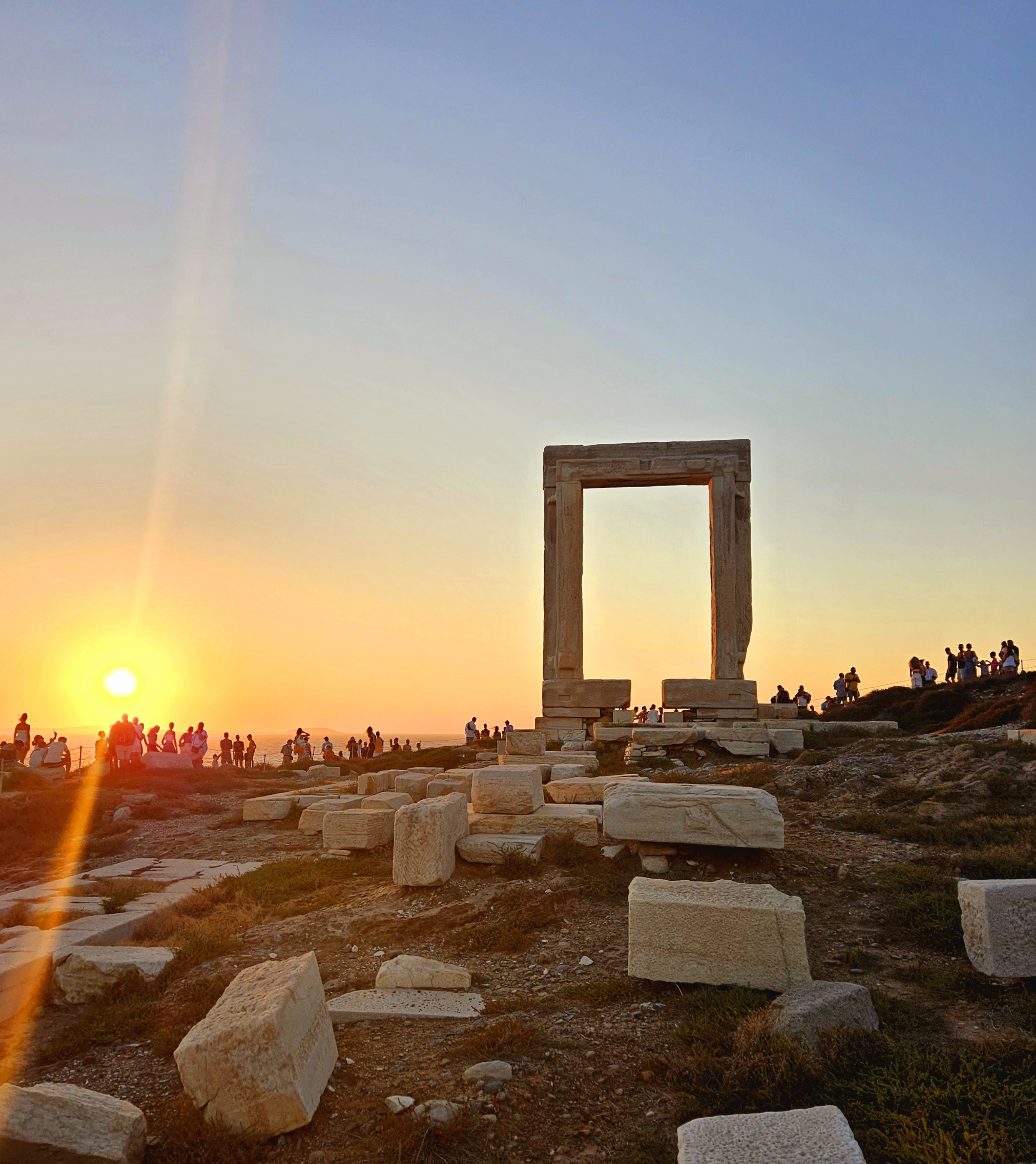 Solnedgång vid det antika Portara, Naxos portalruin i Grekland, med människor som beundrar utsikten.