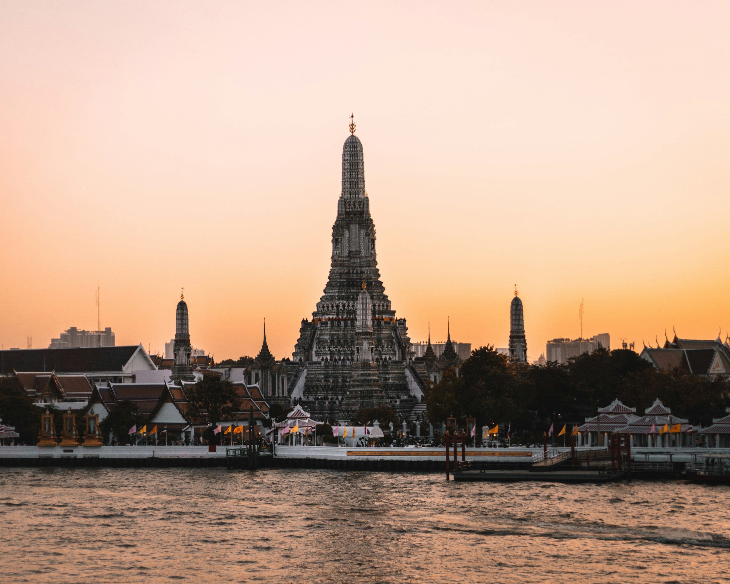 Skymning över ett vackert tempel vid vattnet i Bangkok mot en orange himmel