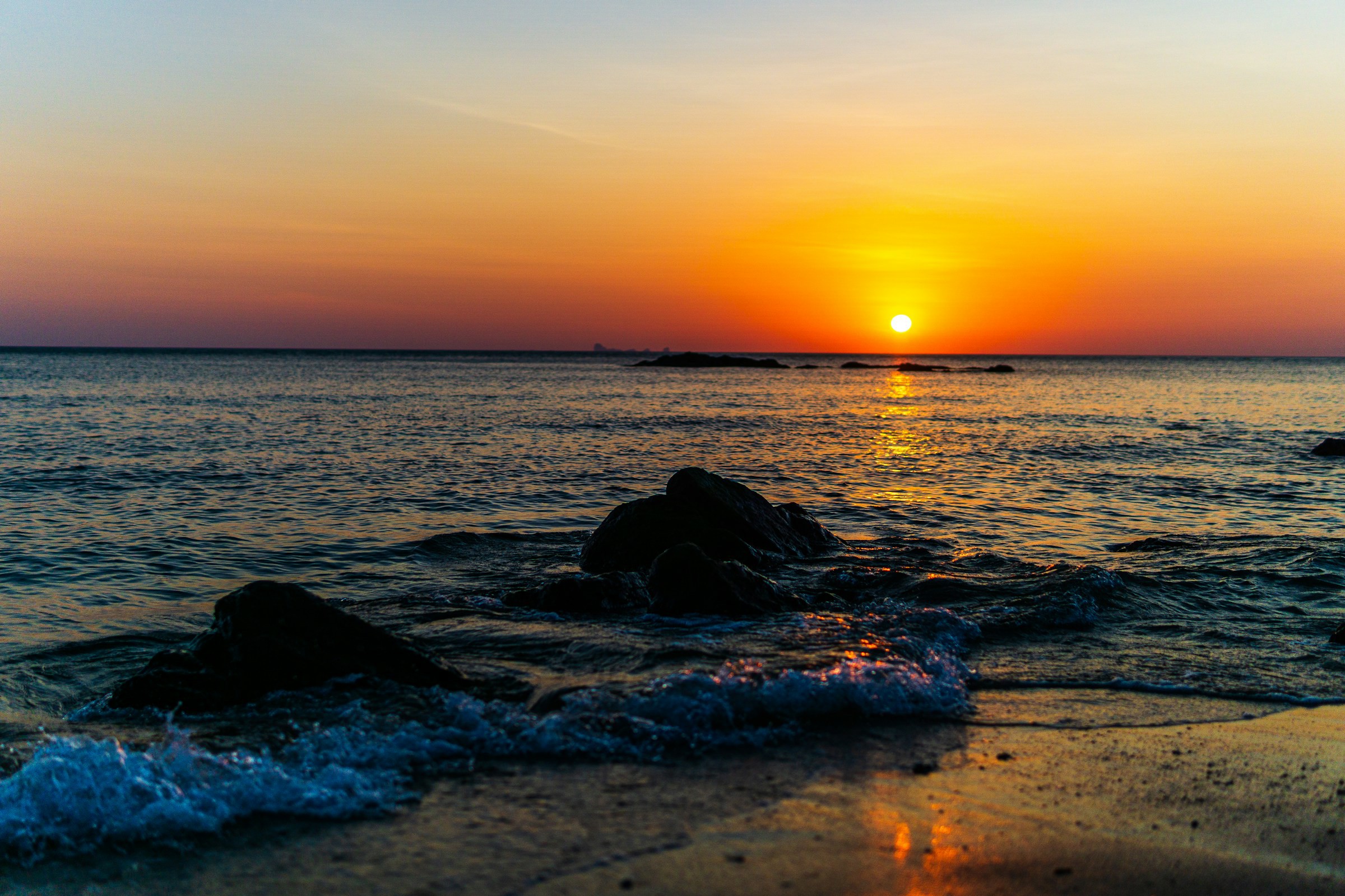 Solnedgång på en strand vid havet med en orange sol som går ner vid horisonten i Koh Lanta, Thailand