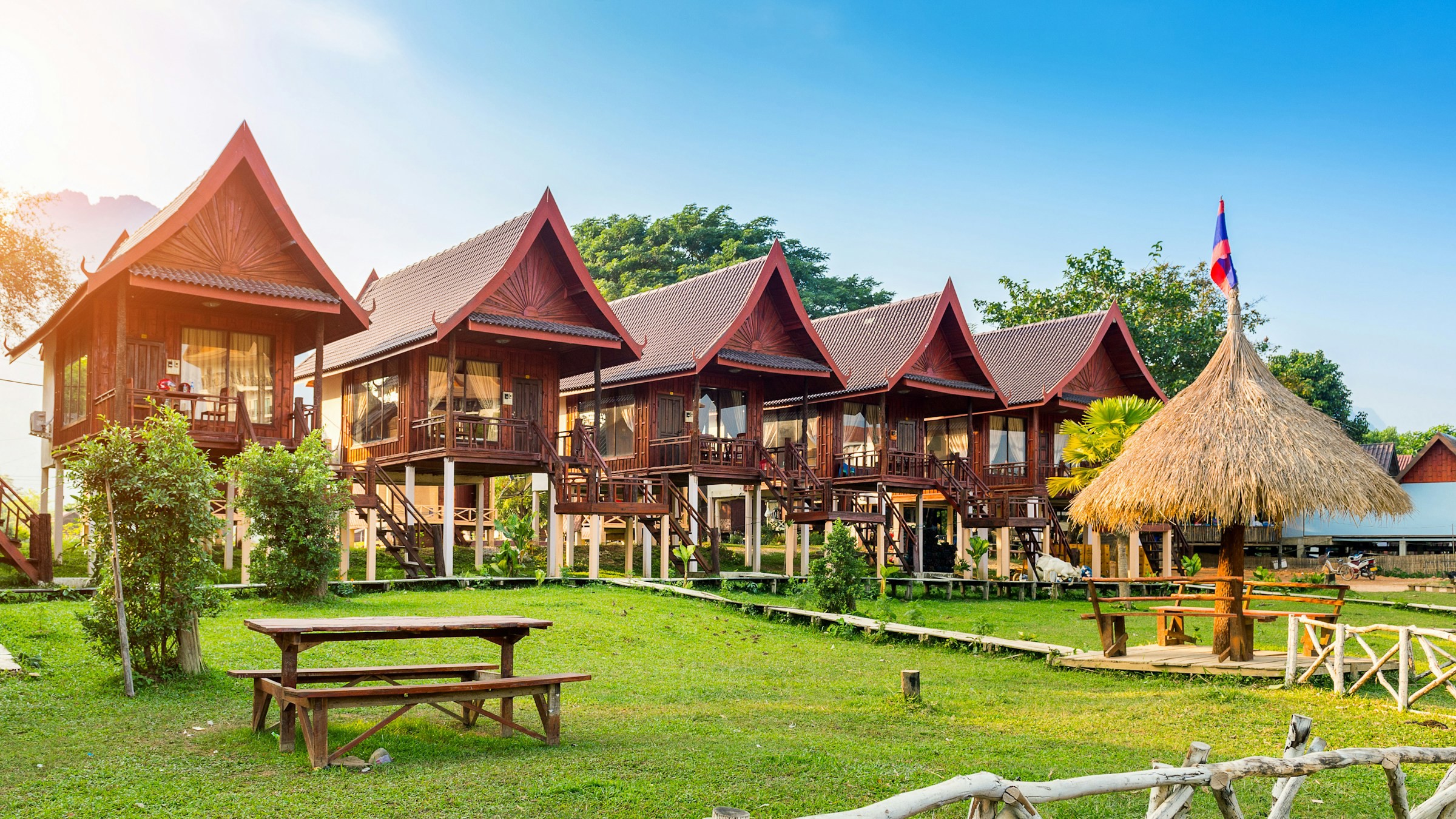 Vackera traditionella byggnader på en gräsmatta vid ett resort och hotell i Phuket med blå himmel i bakgrunden