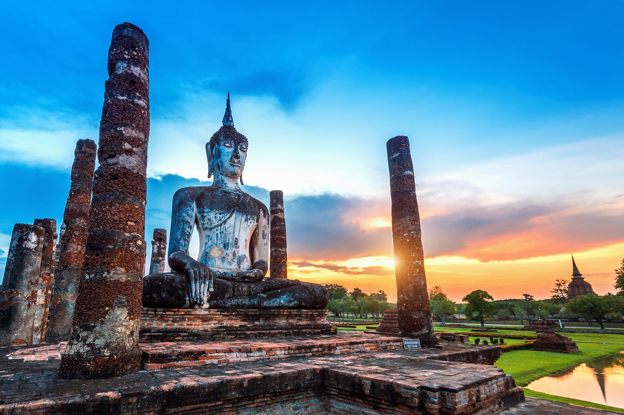 En buddhastaty på en höjd med natur omkring sig under skymning i Thailand