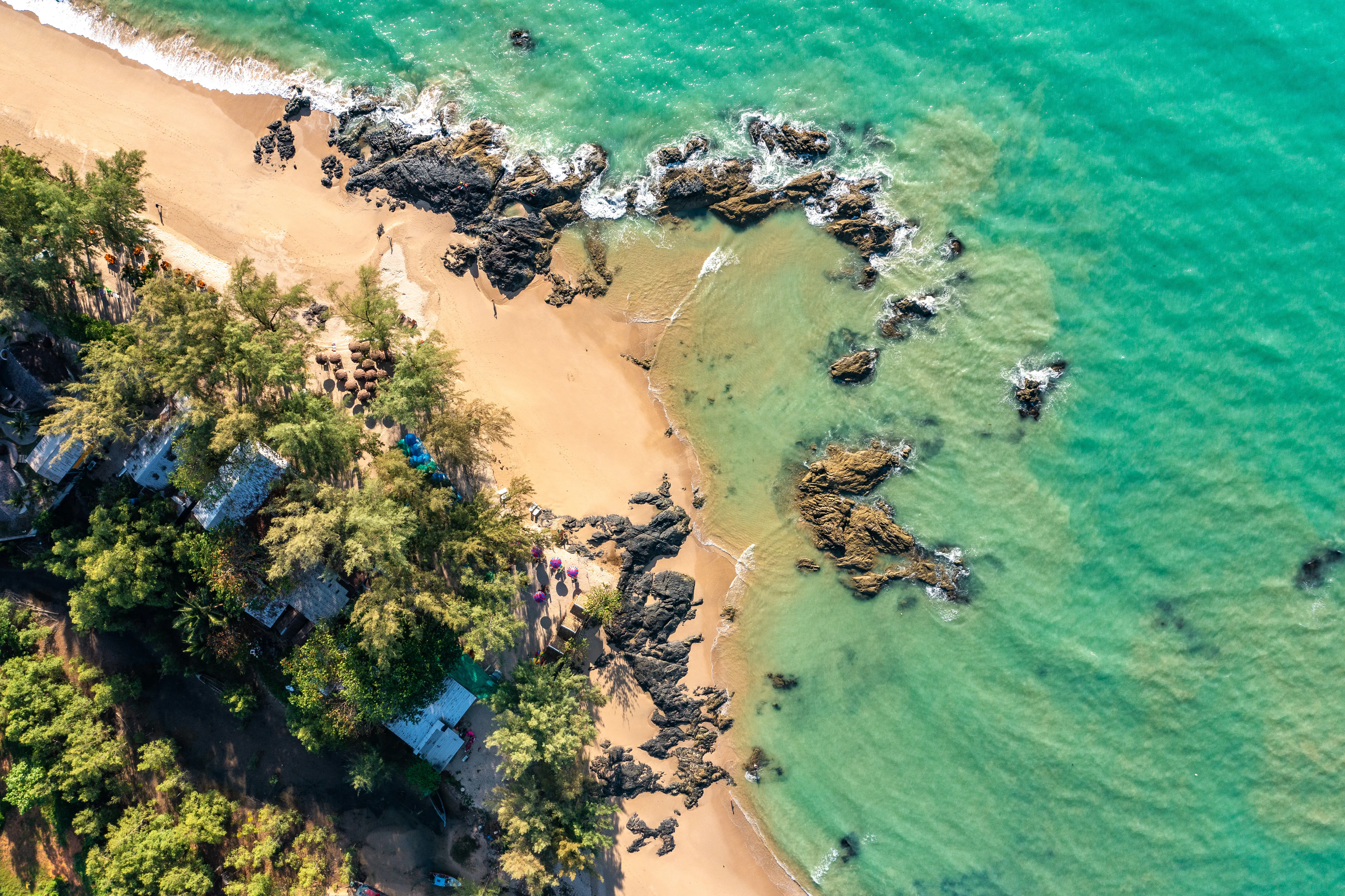 Resa till Khao Lak - Flygbild över en tropisk strand med kristallklart vatten, klippformationer och grönskande vegetation.