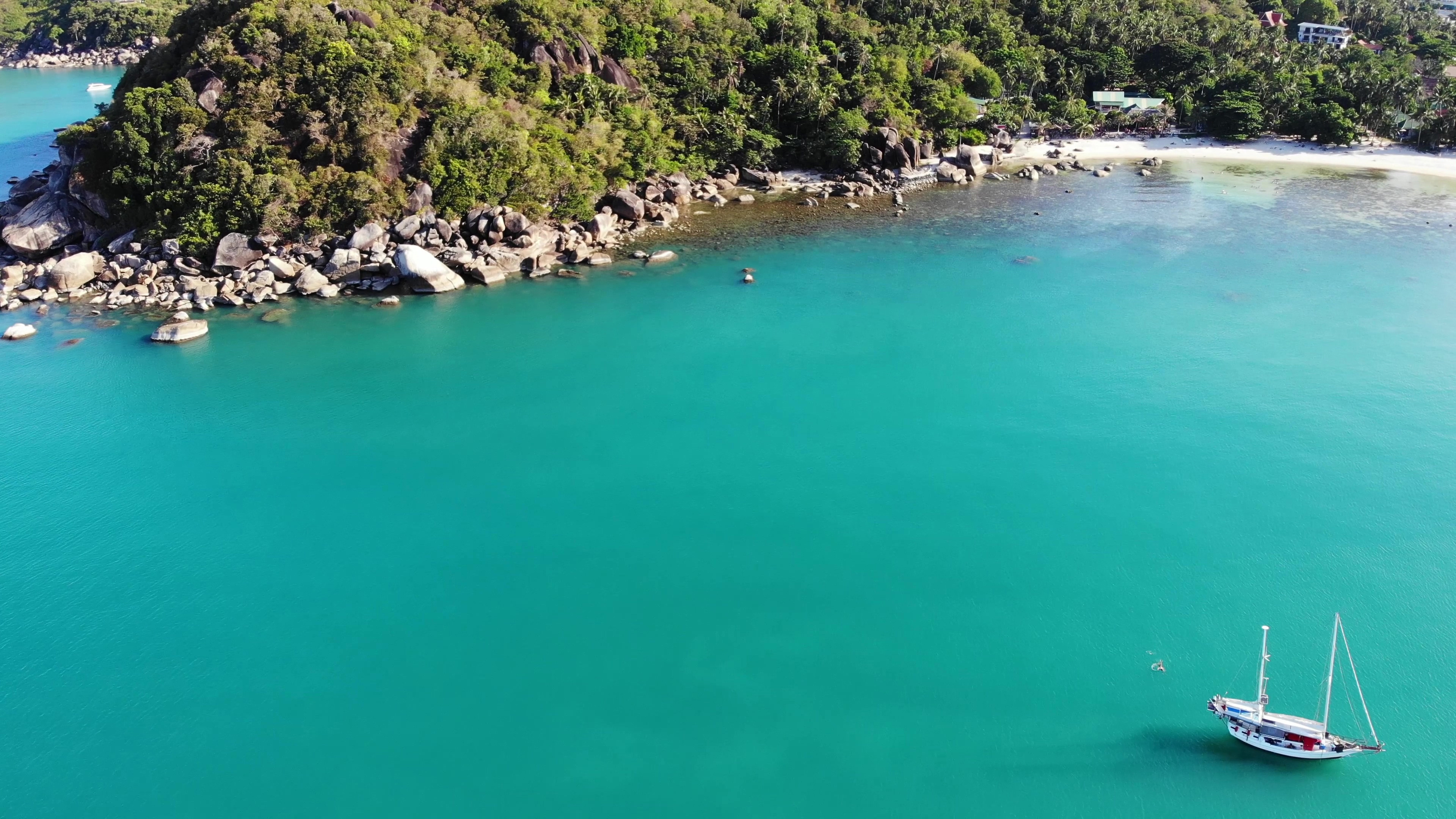 Turkosblått hav med en ensam båt mot en strand och djungel på Koh Samui