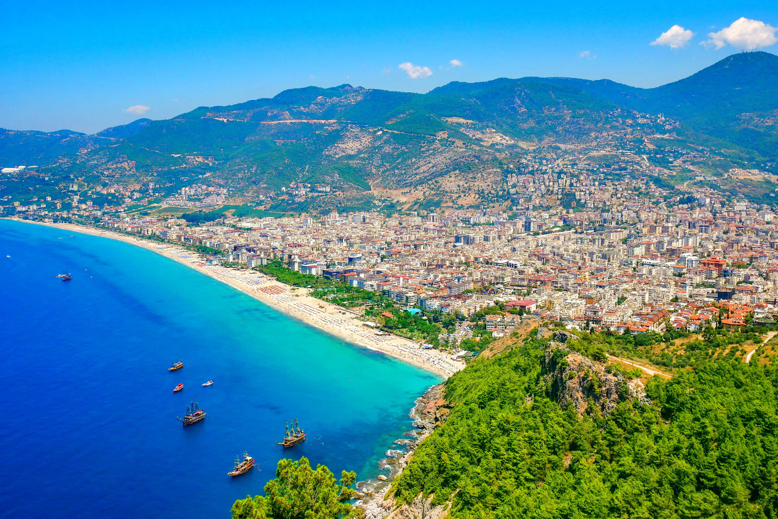 Utsikt över Alanya-stad och stadens strand som möts av klarblått hav med berg i bakgrunden