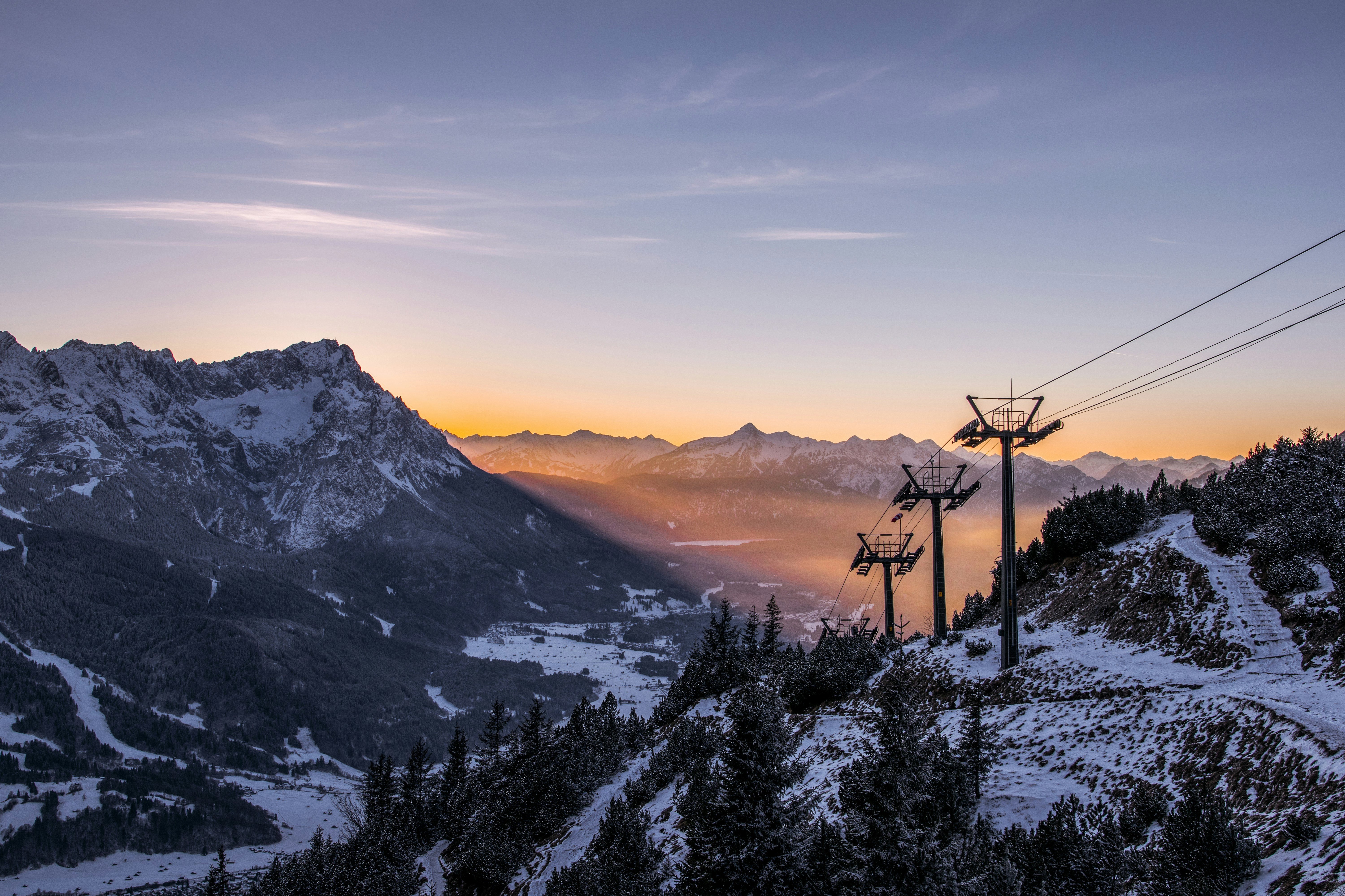 Solnedgång mellan topparna av snötäckta berg och en lift i mitten för skidåkning