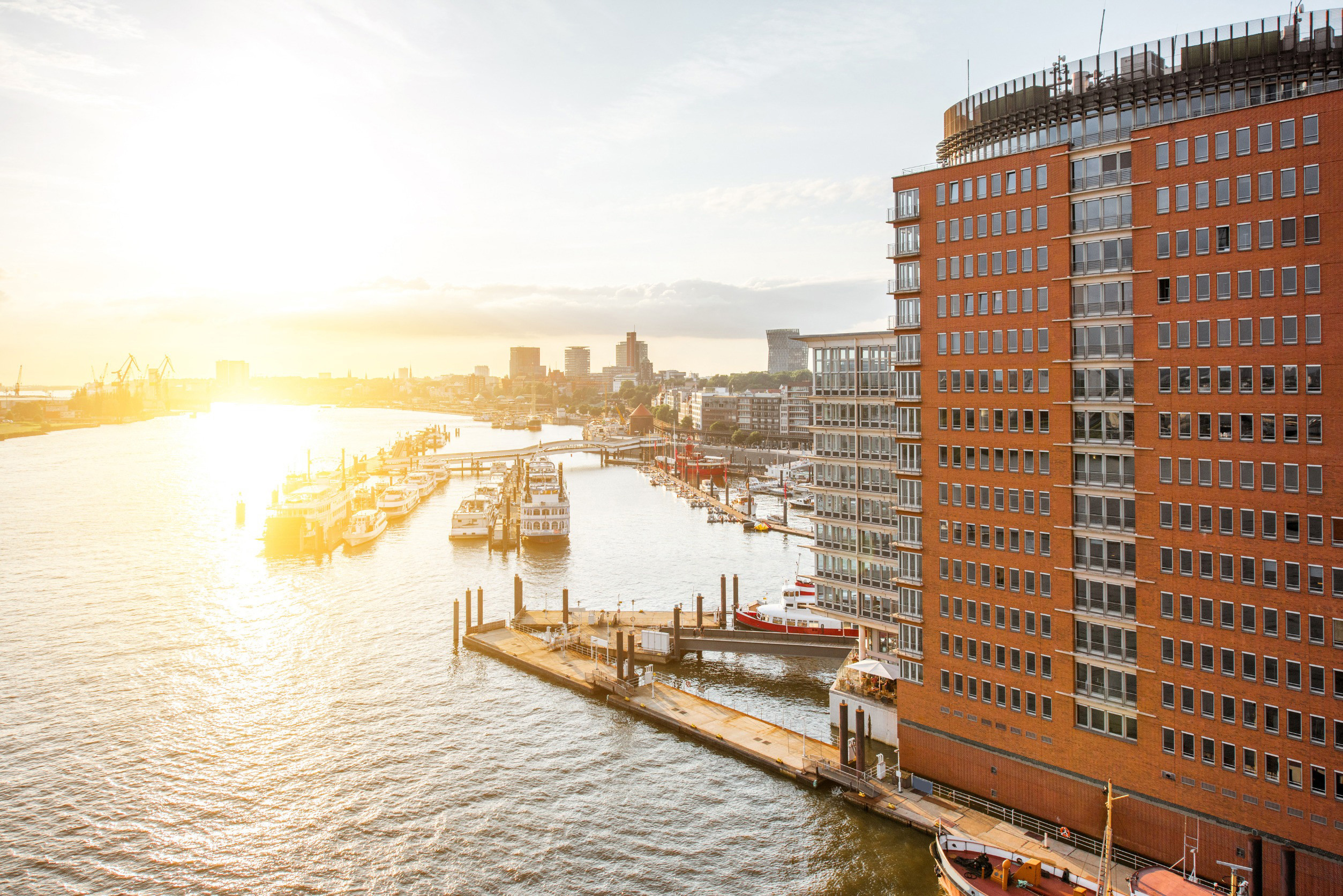 Soluppgång vid en hamn med vatten, båtar och en tegelbyggnad i Hamburg