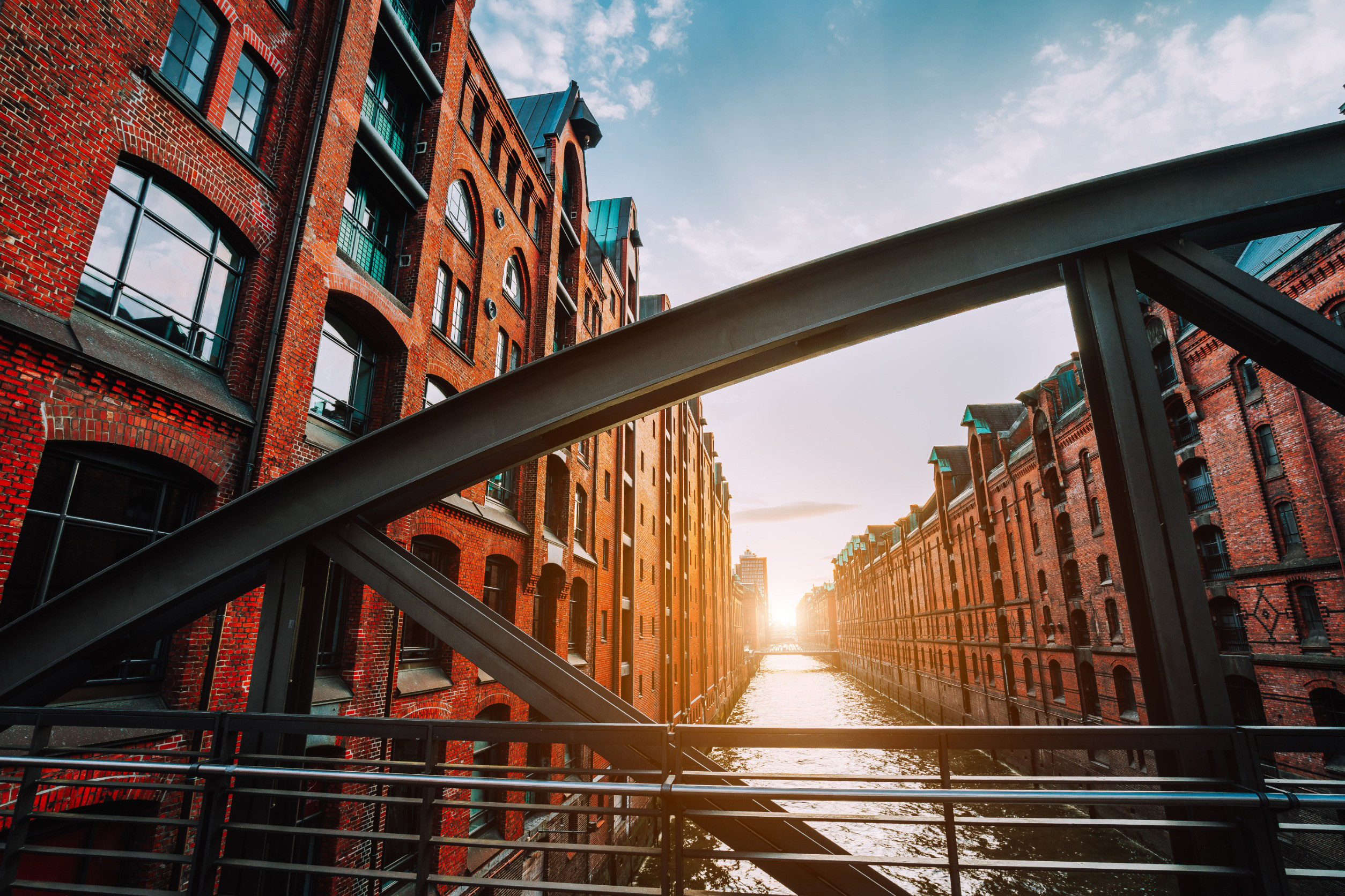 En bro går mellan tegelbyggnader och flod med en solnedgång i bakgrunden i Hamburg