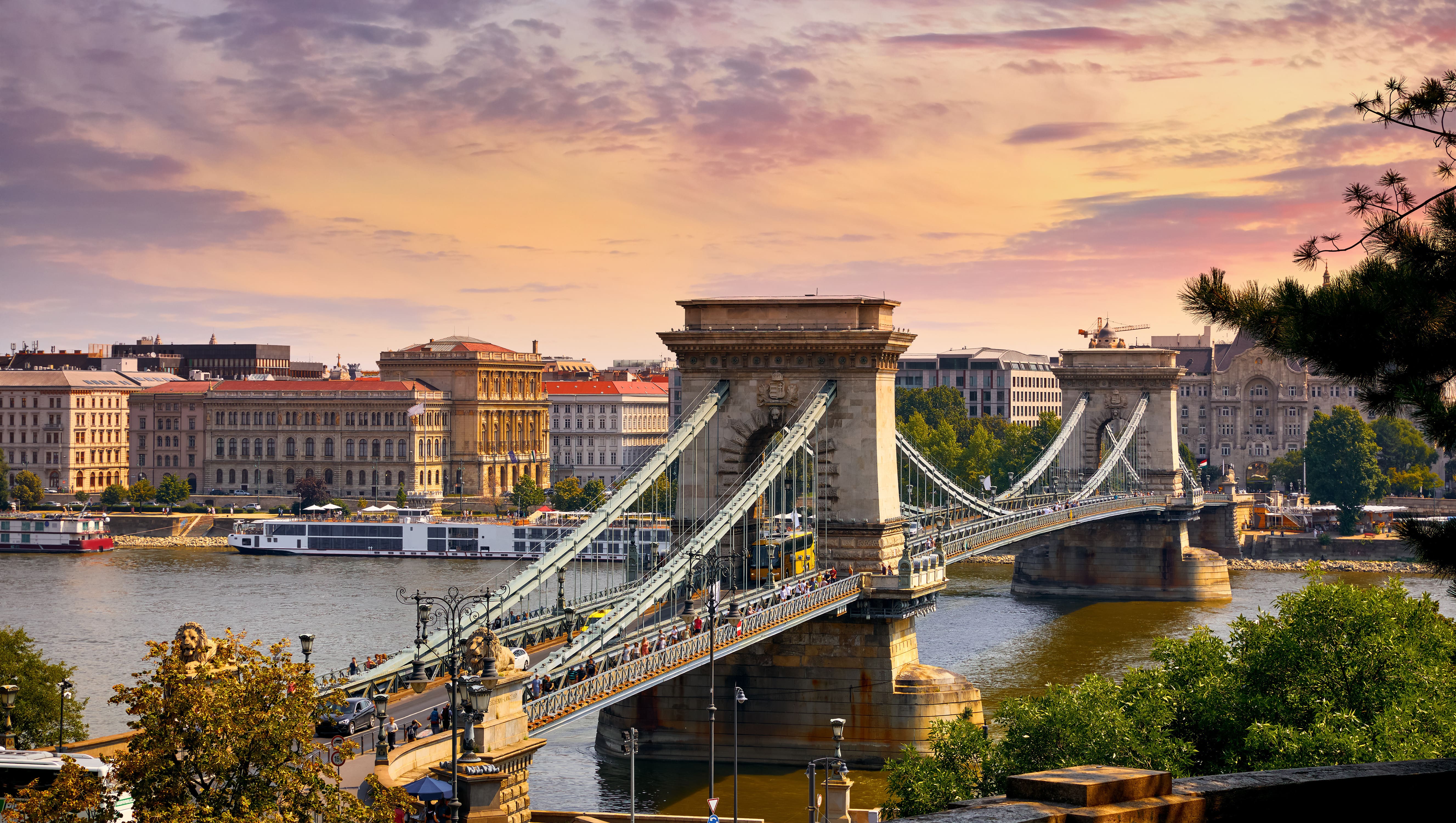 Resa till Budapest - Solnedgång över känd bro över flod i central Budapest med byggnader och vacker himmel i bakgrunden