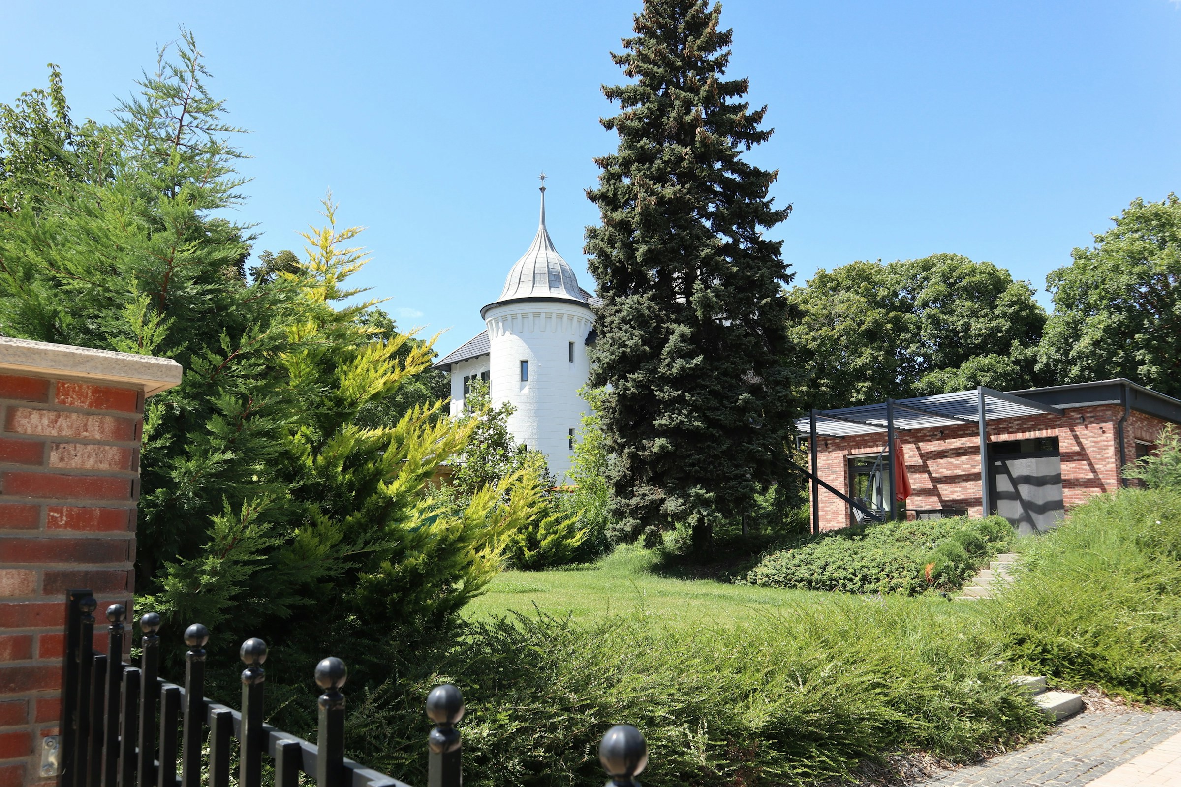 Grönskande trädgård med träd och vit tornbyggnad i bakgrunden på tomten i Ungern