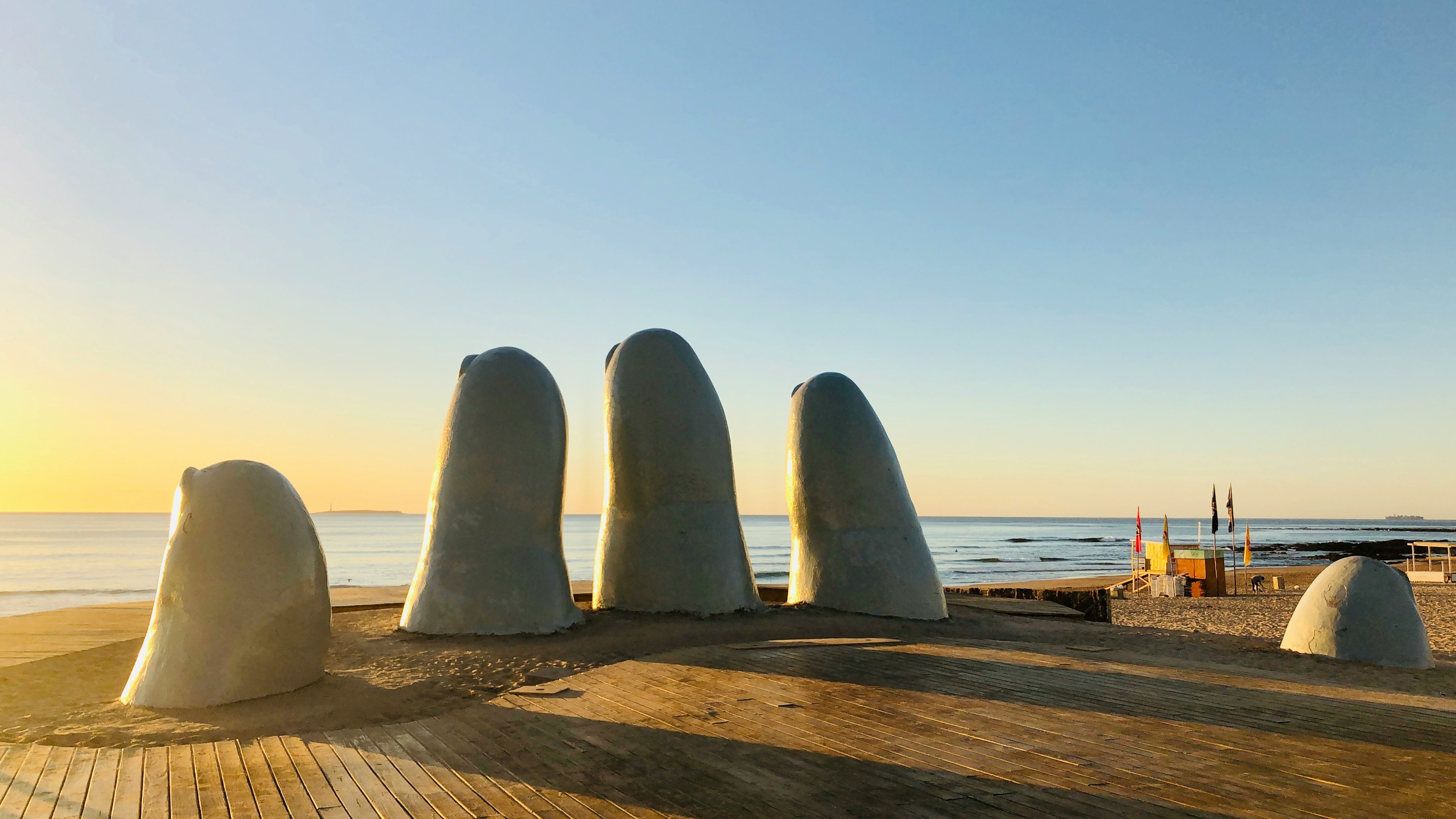 Stor hand i sten kommer ur sanden på en strand i Uruguay under en solnedgång med havet i bakgrunden