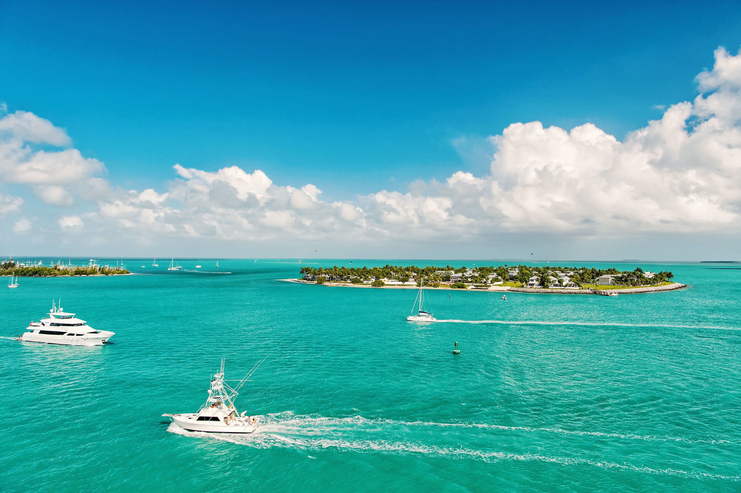 Klart turkosblått vatten med båtar och en liten ö i bakgrunden möter en blå himmel i utkanten av Florida