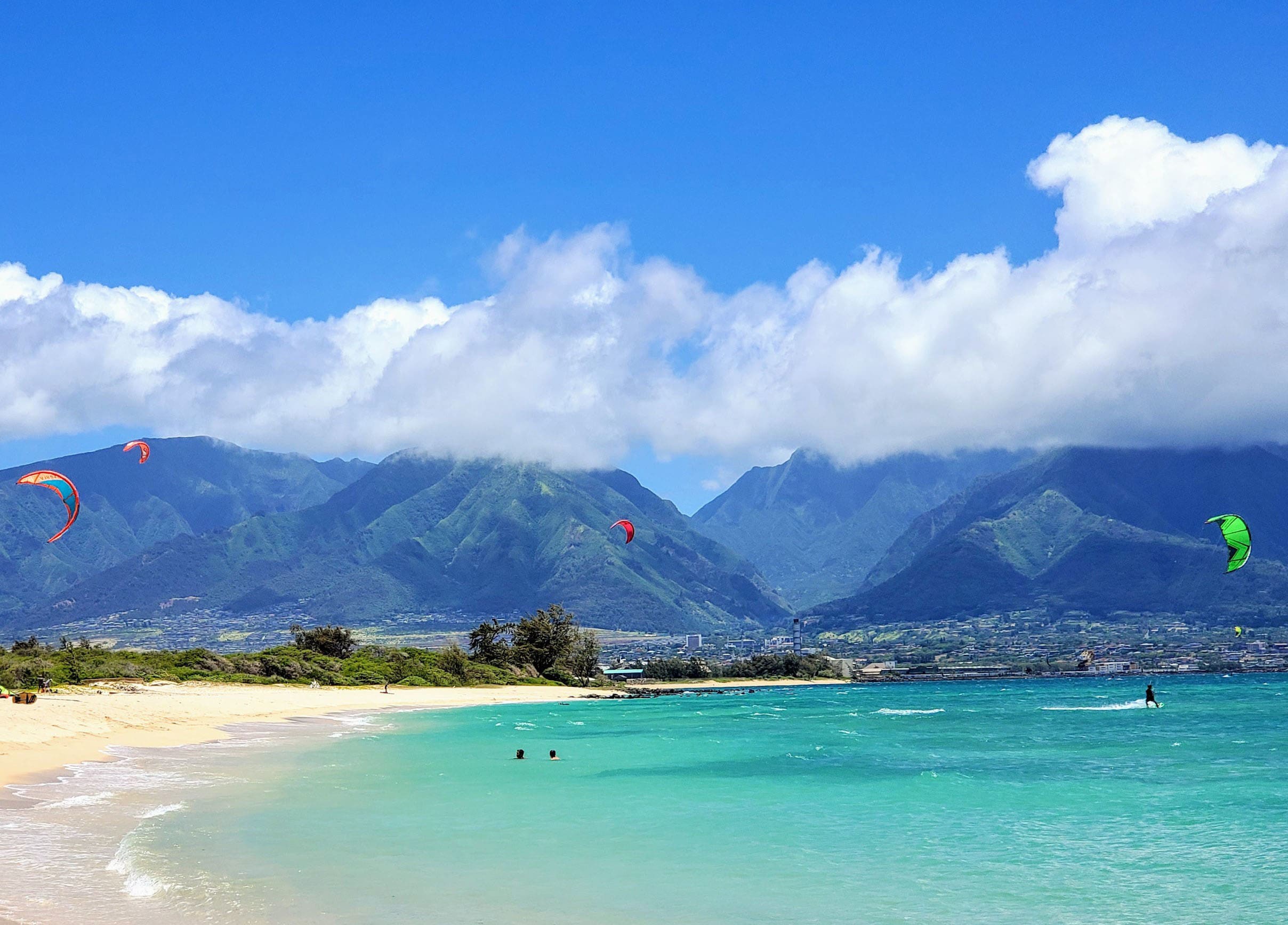 Vacker vit strand och klarblått hav möts av dramatiska berg i bakgrunden på Hawaii