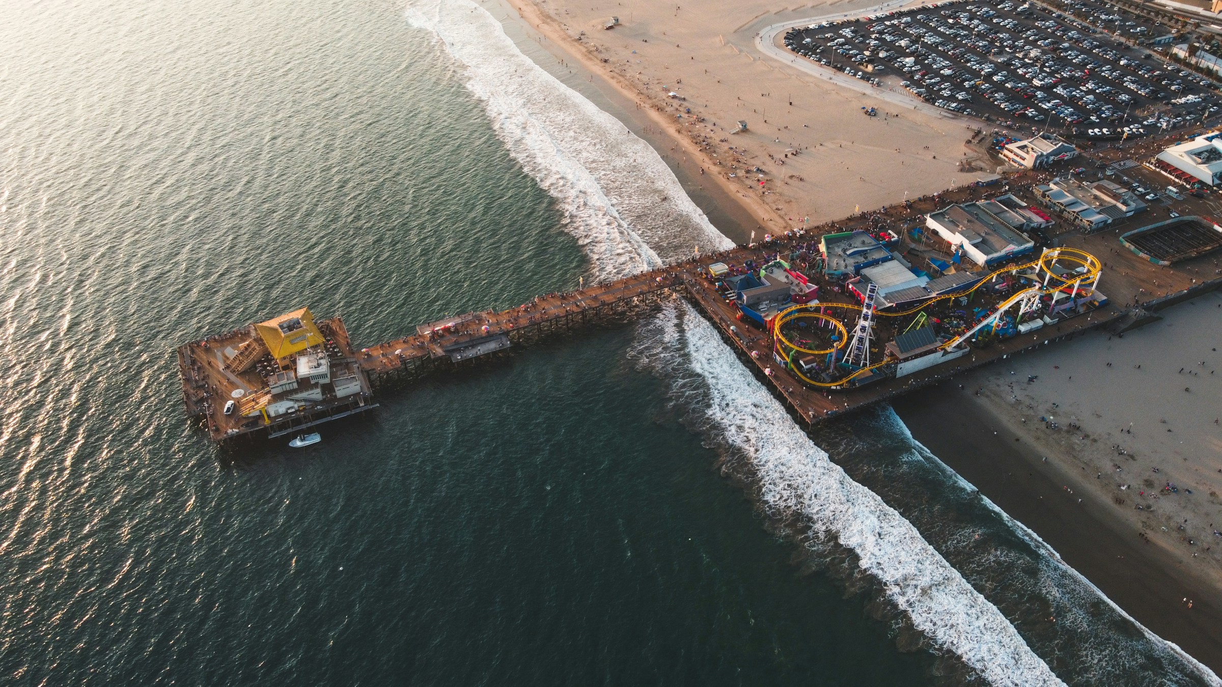 Fågelvy på piren i Santa Monica, Los Angeles som går från en stor strand ut i vattnet och har en nöjespark