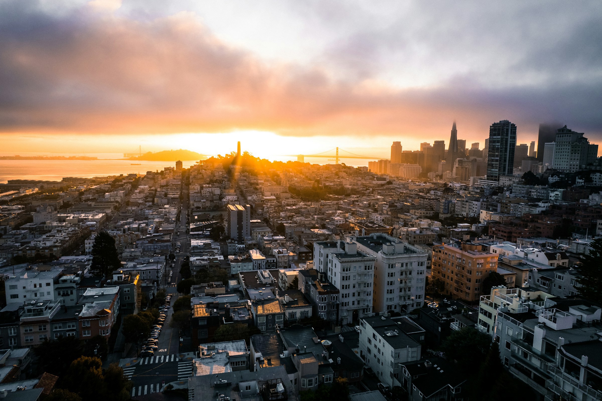 Solnedgång över San Francisco stad med massa byggnader och skyskrapor i bakgrunden mot en orange himmel