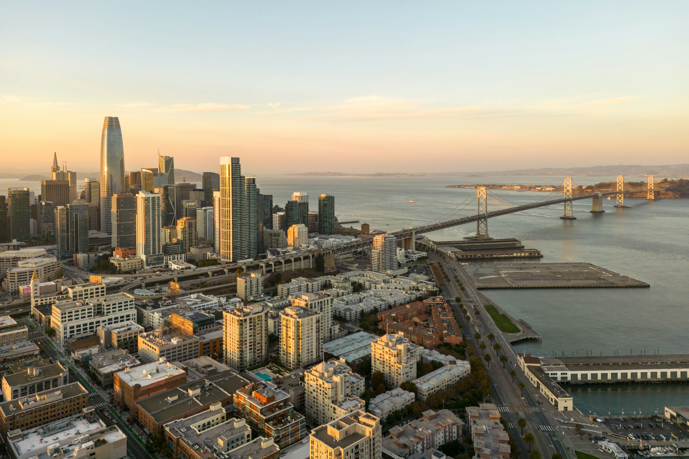 Tidig solnedgång över San Francisco med skyline i bakgrunden mot en blå och orange himmel med hav och broar 