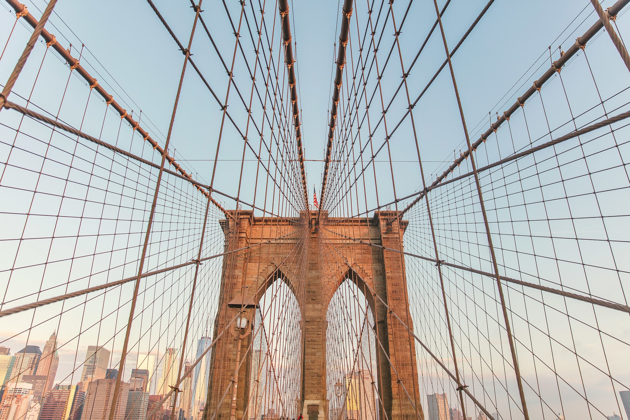 Vy underifrån upp mot ikoniska Brooklyn Bridge i New York med Brooklyn i bakgrunden