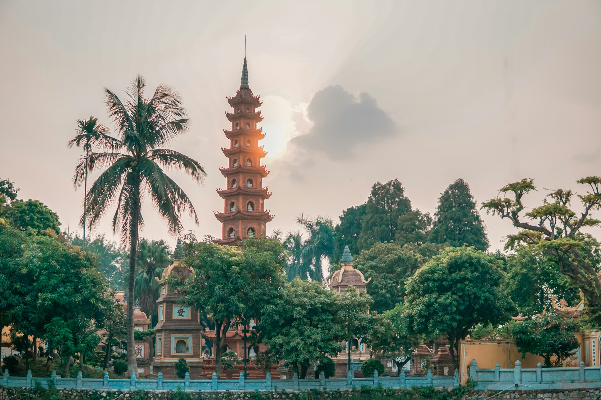 Traditionellt asiatiskt pagodtorn i en frodig trädgård med palmer vid solnedgång i Hanoi.