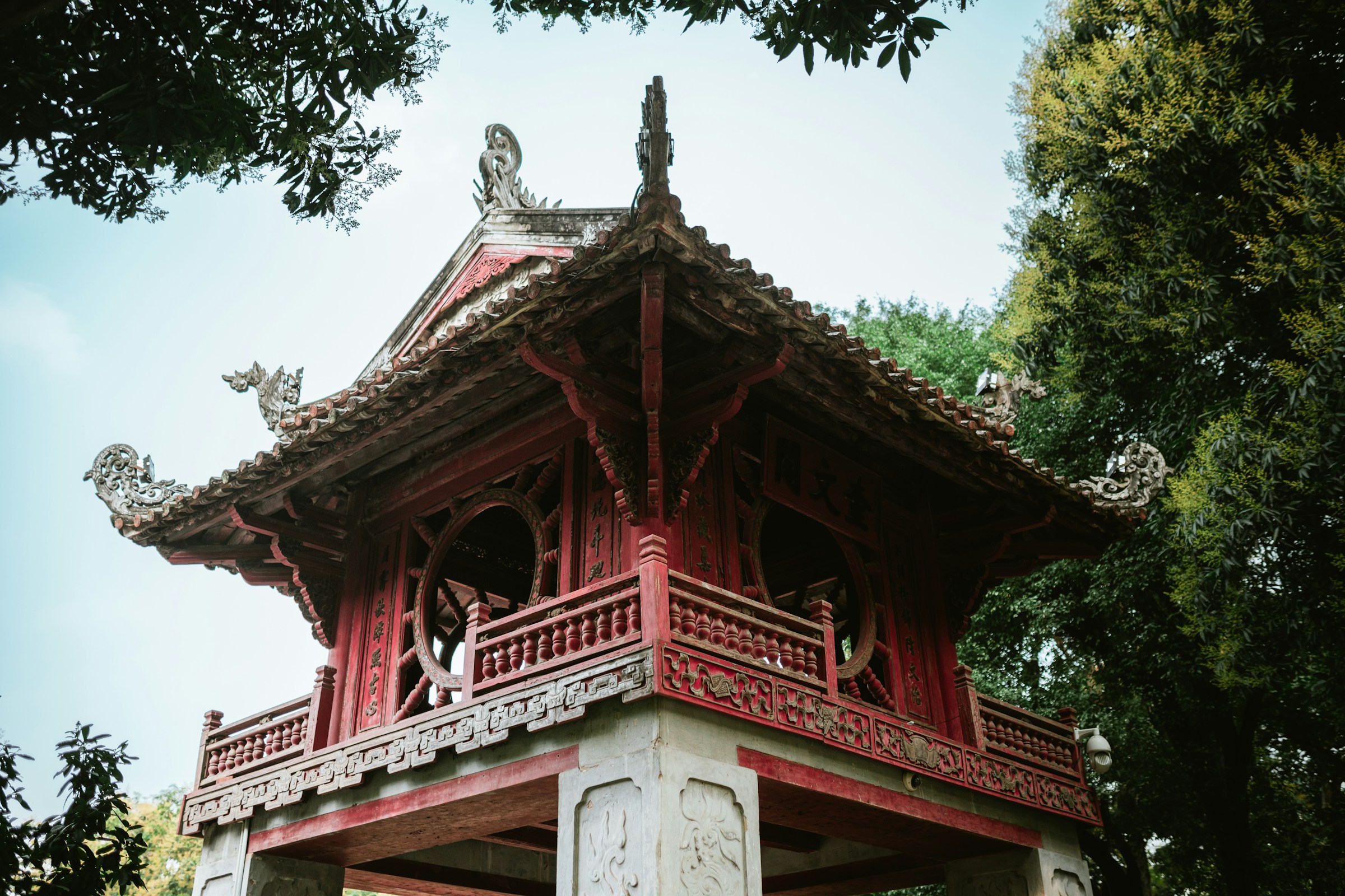 Traditionellt rött tempel med snidade takdetaljer omgivet av grönska i Vietnam.
