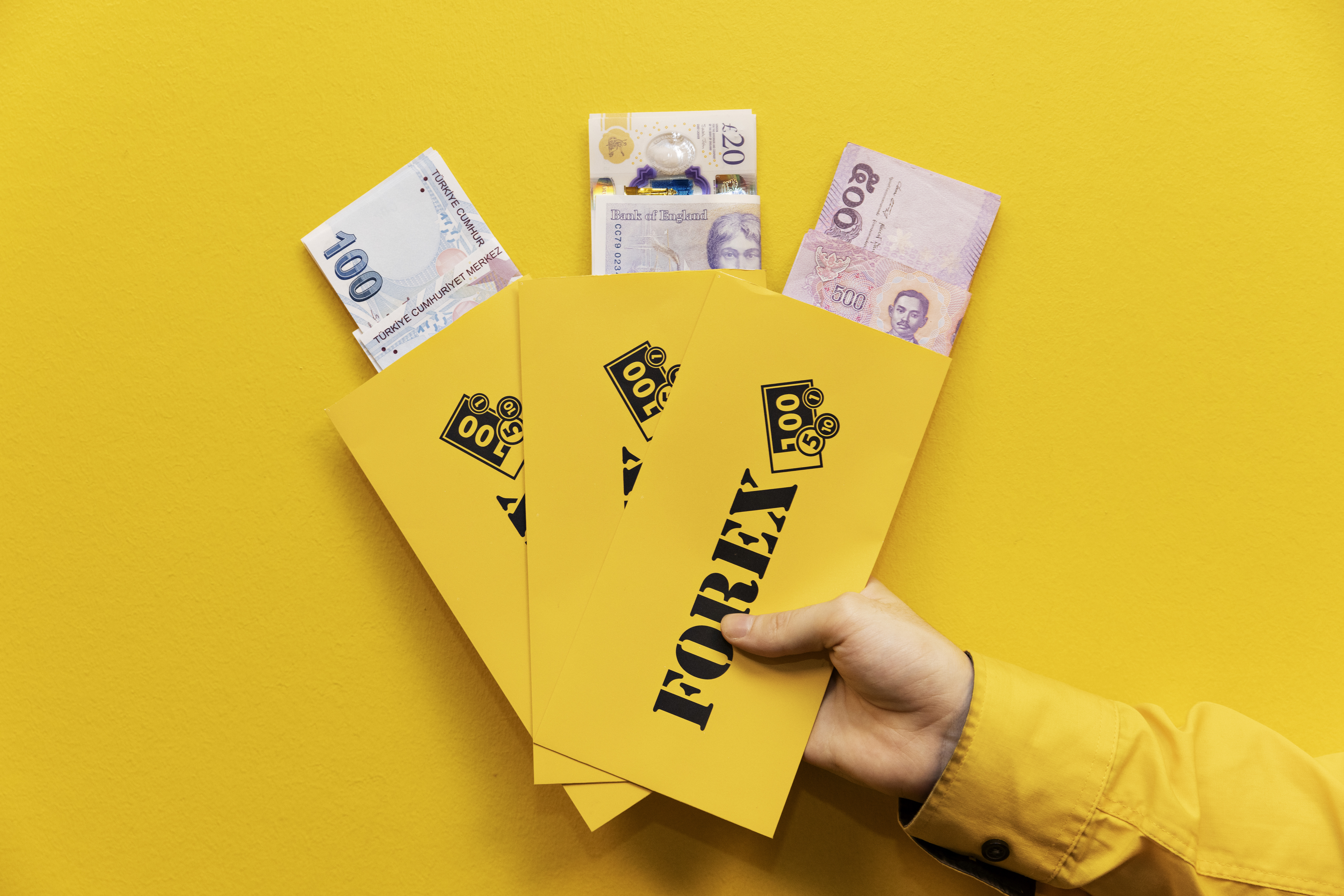 Hand håller gula FOREX kuvert med valuta i olika sedlar mot gul bakgrund.