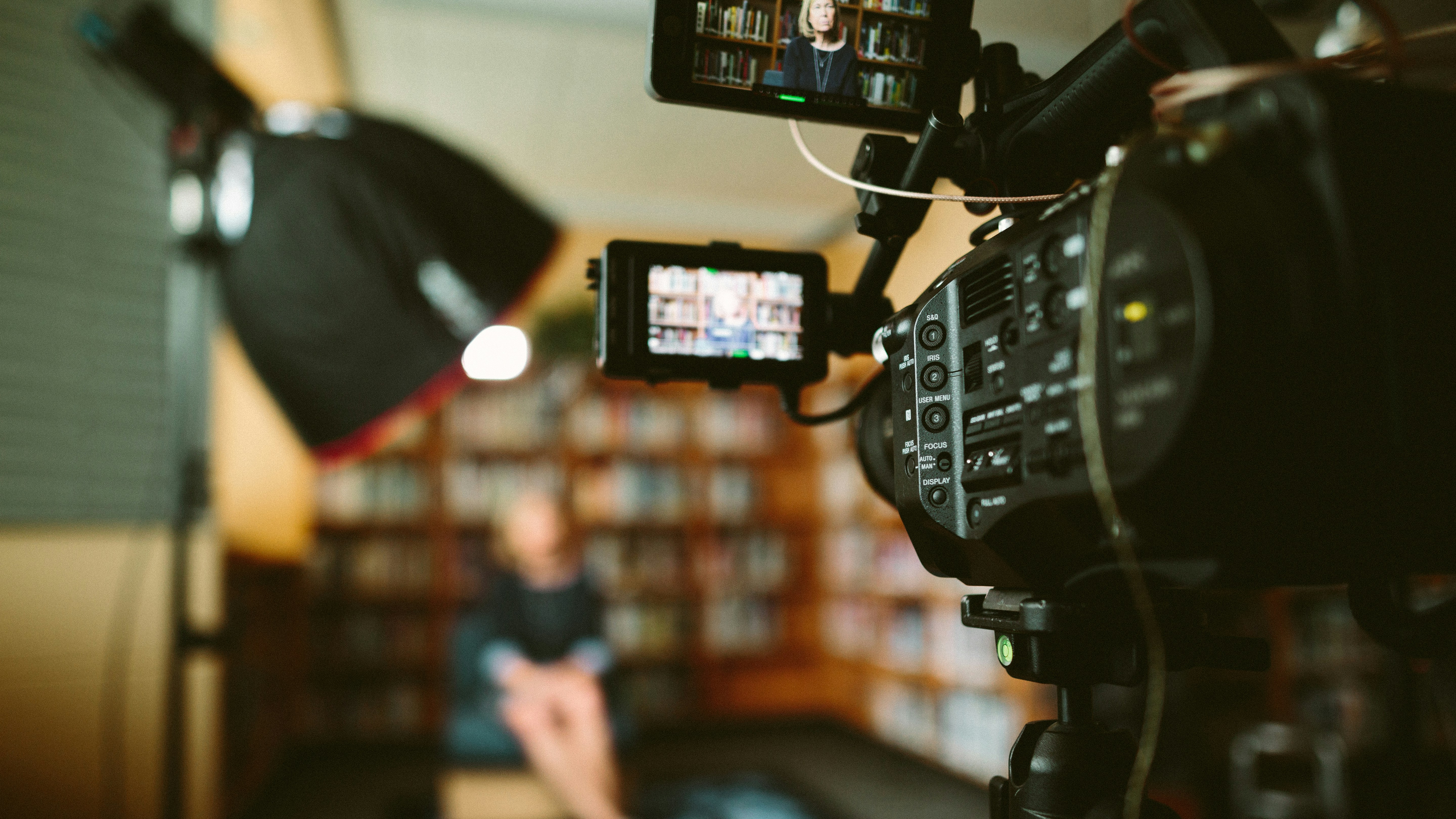 Professionell videofilmning av intervju i bibliotek, kamera utrustning i förgrunden med oskarp person i bakgrunden.